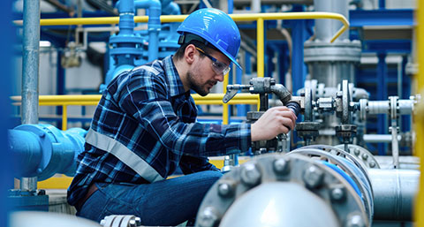 a man in a blue helmet performing maintenance on a gas pipe